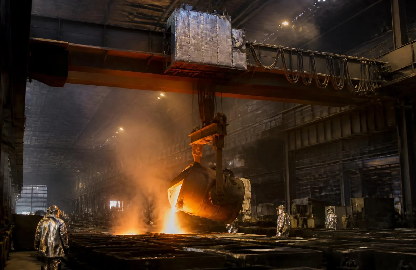 Foundry crane with heat-shielded trolley pouring molten metal from a ladle into sand moulds
