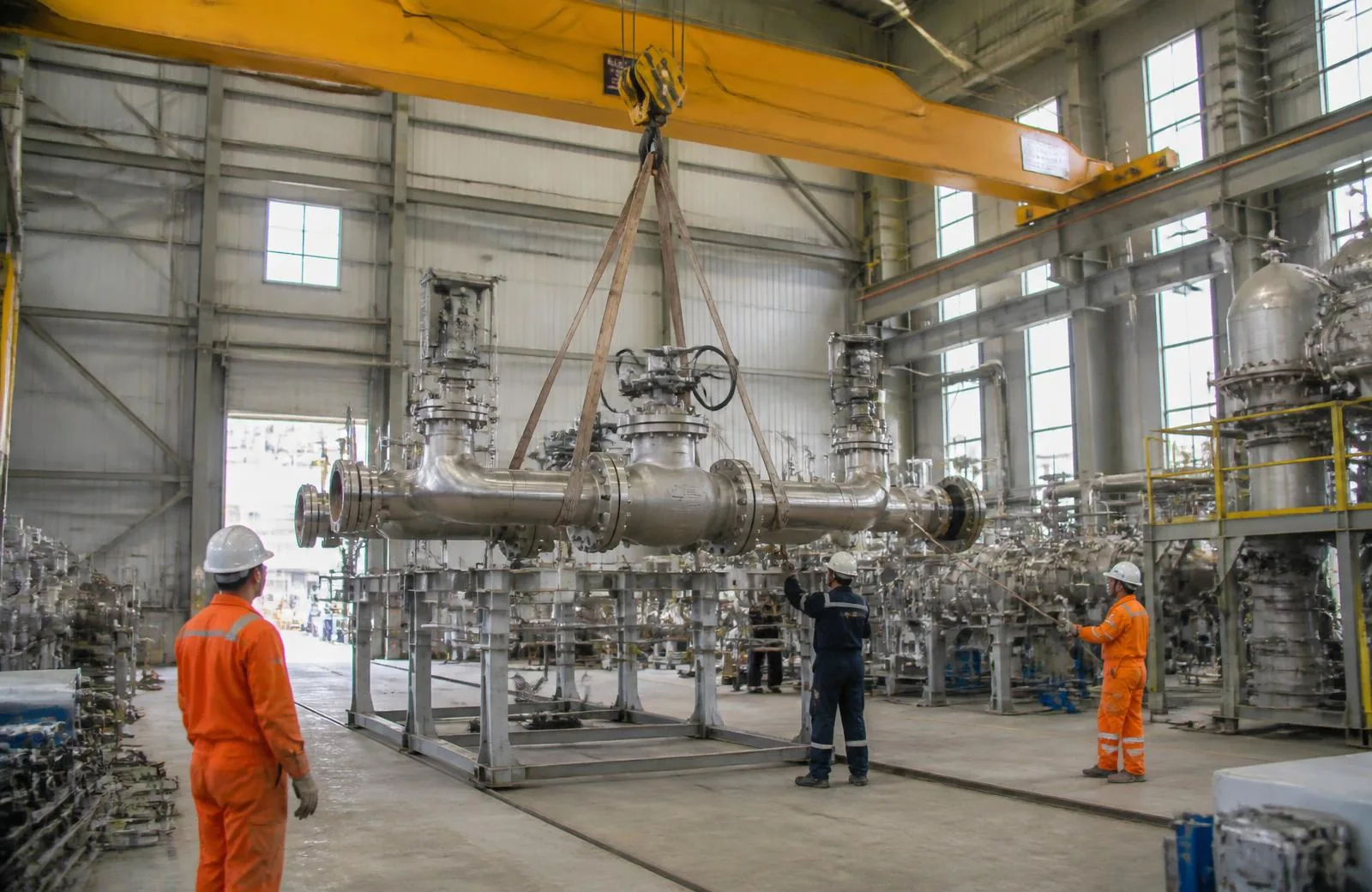 Overhead crane lifting a valve and piping spool in a refinery fabrication shop