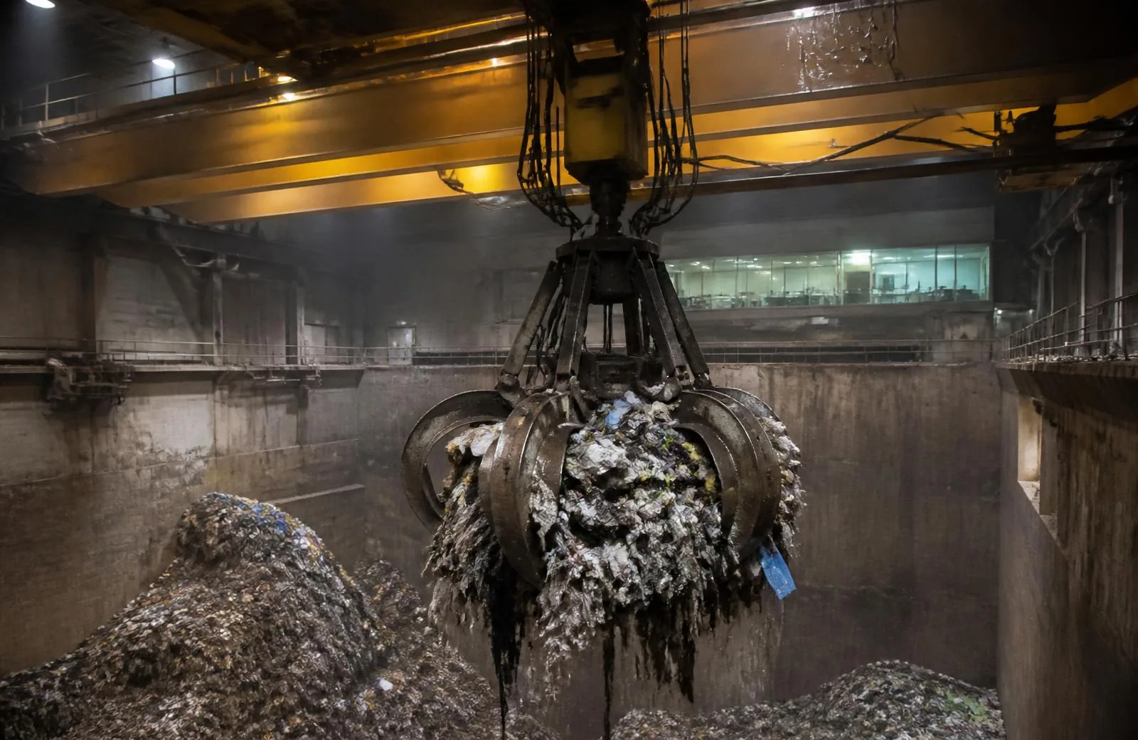 Automated grab crane lifting waste from a refuse bunker at a waste-to-energy plant